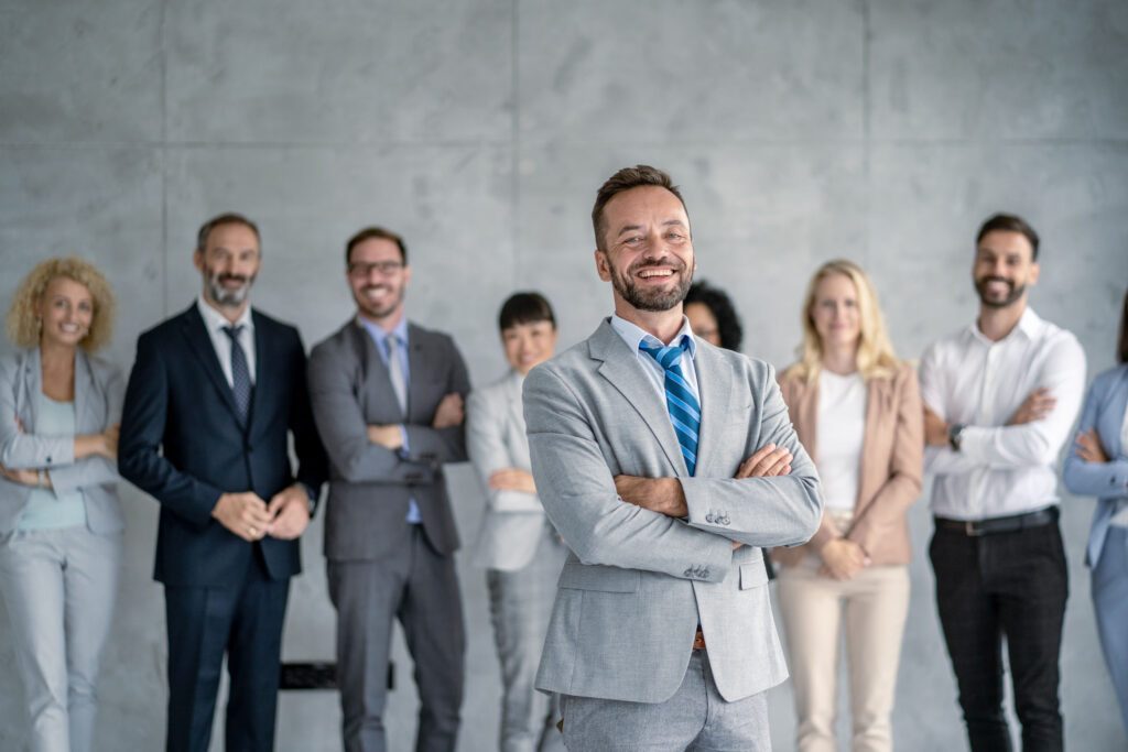 Smiling businessman with arms crossed leading an applauding team.